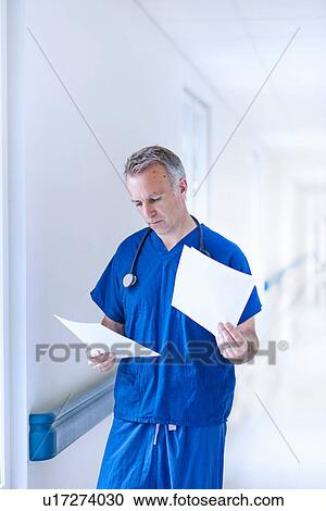 Stock Image - Doctor standing in corridor reading medical records. Fotosearch