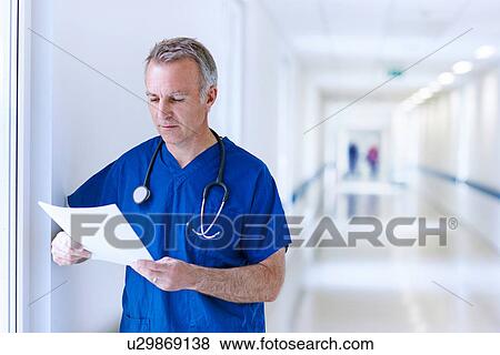 Stock Photo - Doctor standing in corridor reading medical records. Fotosearch