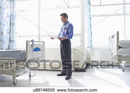 Doctor standing on hospital ward looking at medical records View Large Photo Image Stock Photo - Doctor standing on hospital ward looking at medical records. Fotosearch