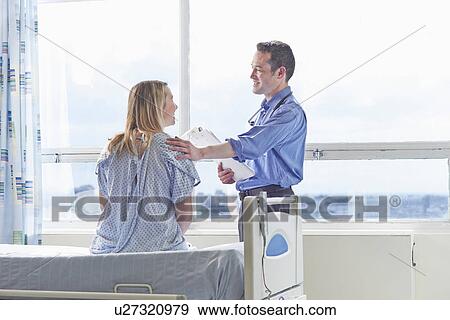 Stock Photo - Doctor talking to patient sitting on hospital bed. Fotosearch