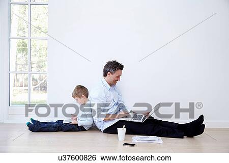Father and son sitting back to back using laptop and digital tablet View Large Photo Image Stock Photograph - Father and son sitting back to back using laptop and digital tablet. Fotosearch