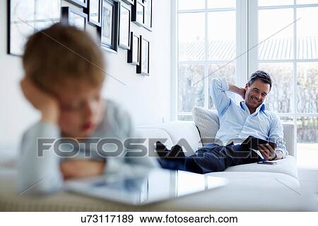 Father and son sitting on sofa using digital tablets View Large Photo Image Stock Photo - Father and son sitting on sofa using digital tablets. Fotosearch