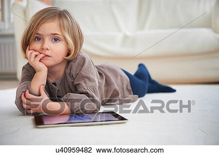 Stock Image - Girl lying on floor using digital tablet. Fotosearch