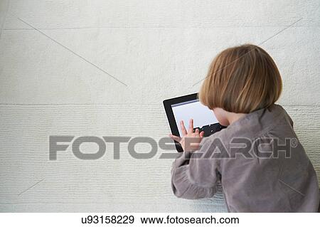 Girl lying on floor using digital tablet View Large Photo Image Stock Photo - Girl lying on floor using digital tablet. Fotosearch