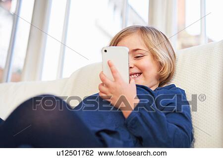 Stock Image - Girl on sofa using smartphone. Fotosearch