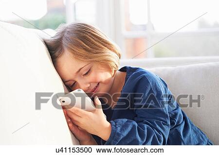 Stock Image - Girl on sofa using smartphone. Fotosearch