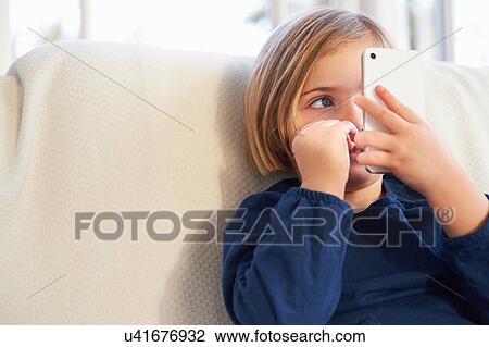 Stock Image - Girl on sofa using smartphone. Fotosearch