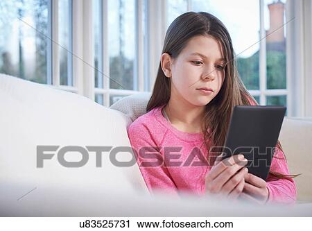 Stock Image - Girl using digital tablet on sofa. Fotosearch