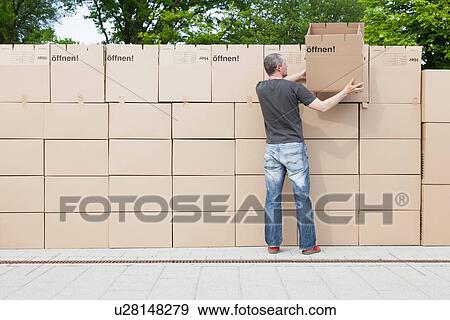 Stock Photo - Man building wall of cardboard boxes. Fotosearch