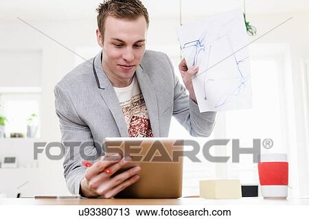 Stock Image - Man holding up sketch in front of digital tablet. Fotosearch