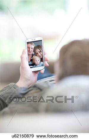 Man looking at family photo on cellphone View Large Photo Image Stock Photo - Man looking at family photo on cellphone. Fotosearch