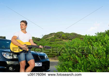 Picture - Man playing guitar leaning against car. Fotosearch