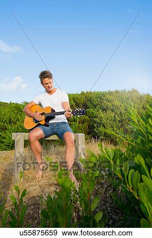 Man playing guitar on wooden bench View Large Photo Image Stock Photo - Man playing guitar on wooden bench. Fotosearch