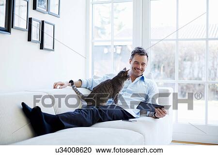 Man relaxing on sofa using digital tablet with cat View Large Photo Image Stock Image - Man relaxing on sofa using digital tablet with cat. Fotosearch