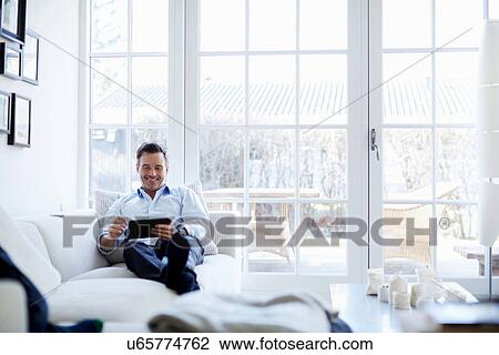 Stock Image - Man relaxing on sofa using digital tablet. Fotosearch