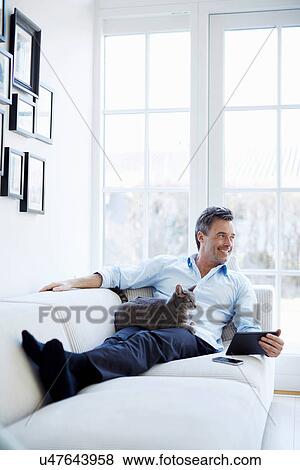 Man relaxing on sofa using digital tablet with cat View Large Photo Image Stock Photo - Man relaxing on sofa using digital tablet with cat. Fotosearch