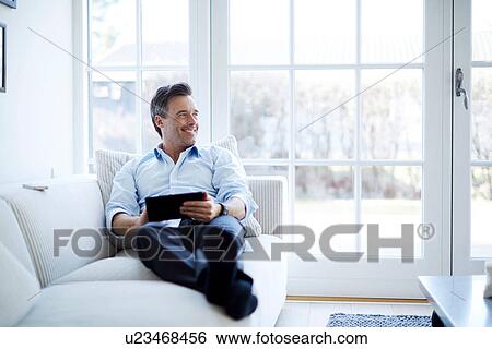 Man relaxing on sofa using digital tablet View Large Photo Image Stock Photograph - Man relaxing on sofa using digital tablet. Fotosearch