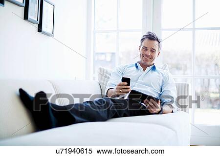 Man relaxing on sofa using digital tablet and smartphone View Large Photo Image Stock Photography - Man relaxing on sofa using digital tablet and smartphone. Fotosearch