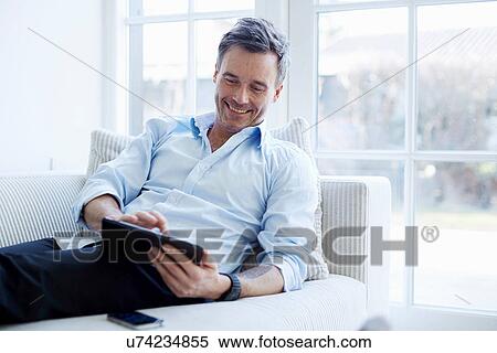Stock Photography - Man relaxing on sofa using digital tablet. Fotosearch