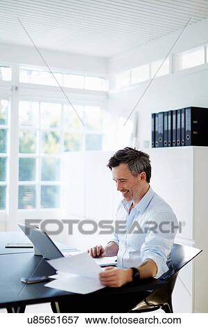 Man sitting at desk with laptop computer and paperwork View Large Photo Image Stock Photo - Man sitting at desk with laptop computer and paperwork. Fotosearch