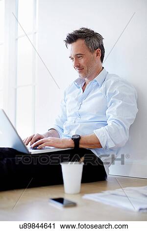 Stock Image - Man sitting on floor sing laptop. Fotosearch