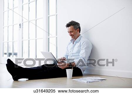 Stock Photography - Man sitting on floor sing laptop. Fotosearch