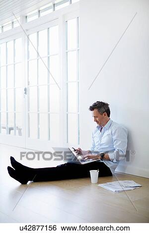 Man sitting on floor using laptop and phone View Large Photo Image Stock Photograph - Man sitting on floor using laptop and phone. Fotosearch