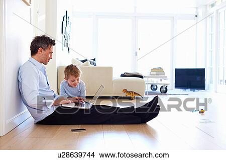 Man sitting on floor using laptop, son watching View Large Photo Image Picture - Man sitting on floor using laptop, son watching. Fotosearch