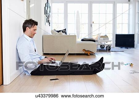 Stock Photograph - Man sitting on floor using laptop. Fotosearch