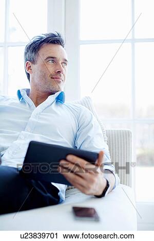 Man sitting on sofa using digital tablet View Large Photo Image Stock Image - Man sitting on sofa using digital tablet. Fotosearch