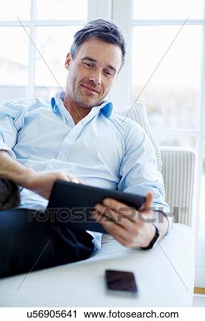 Man sitting on sofa using digital tablet View Large Photo Image Stock Image - Man sitting on sofa using digital tablet. Fotosearch
