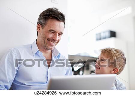 Stock Photograph - Man using laptop, son watching. Fotosearch