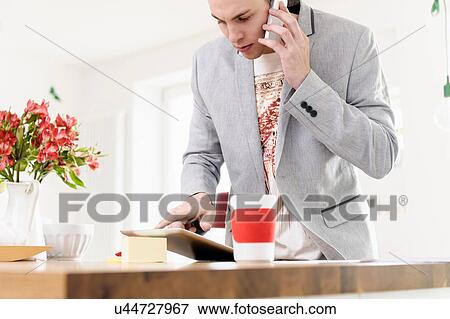 Stock Photo - Man using mobile phone and digital tablet. Fotosearch
