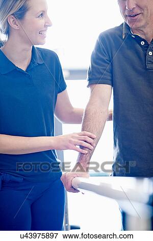 Stock Photo - Man walking supported by rails, guided by therapist. Fotosearch