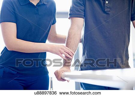 Stock Photograph - Man walking supported by rails, guided by therapist. Fotosearch