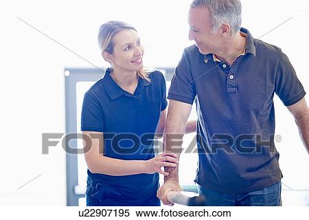 Man walking supported by rails, guided by therapist View Large Photo Image Stock Photography - Man walking supported by rails, guided by therapist. Fotosearch