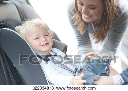 Stock Image - Mother checking baby son in back seat of car. Fotosearch