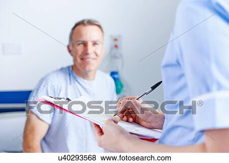 Nurse completing paperwork, patient in background View Large Photo Image Stock Photo - Nurse completing paperwork, patient in background. Fotosearch