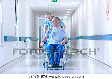 Picture - Nurse pushing patient in wheelchair down corridor. Fotosearch