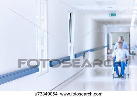 Nurse pushing patient in wheelchair down corridor View Large Photo Image Picture - Nurse pushing patient in wheelchair down corridor. Fotosearch