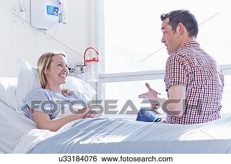 Patient lying in hospital bed talking to visitor View Large Photo Image Stock Photograph - Patient lying in hospital bed talking to visitor. Fotosearch