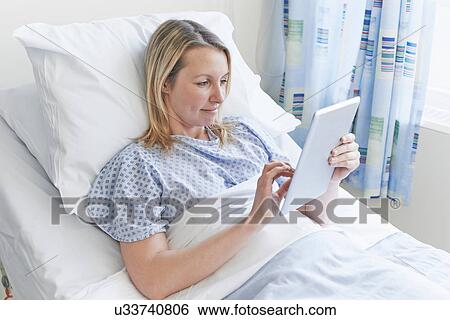 Patient lying on hospital bed using digital tablet View Large Photo Image Stock Photograph - Patient lying on hospital bed using digital tablet. Fotosearch