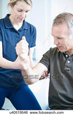 Stock Photograph - Physiotherapist helping man to do arm exercise. Fotosearch