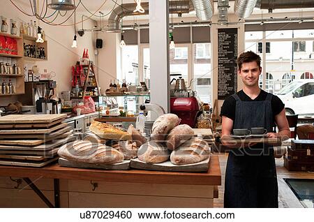 Stock Image - Portrait of young man carrying tray in cafe. Fotosearch