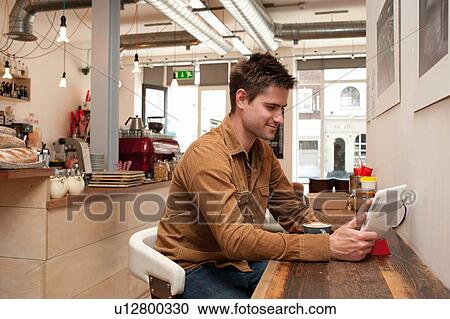 Portrait of young man looking at digital tablet in cafe View Large Photo Image Stock Image - Portrait of young man looking at digital tablet in cafe. Fotosearch