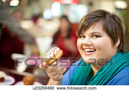 Stock Image - Portrait of young woman holding doughnut. Fotosearch