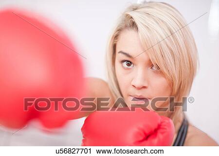 Stock Image - Portrait of young woman wearing boxing gloves. Fotosearch