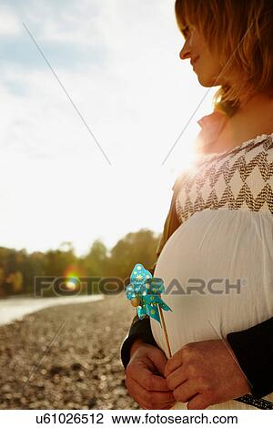 Pregnant woman standing beside river holding windmill View Large Photo Image Stock Image - Pregnant woman standing beside river holding windmill. Fotosearch