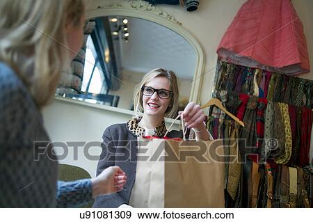 Sales assistant handing shopping bag to lady View Large Photo Image Stock Photo - Sales assistant handing shopping bag to lady. Fotosearch