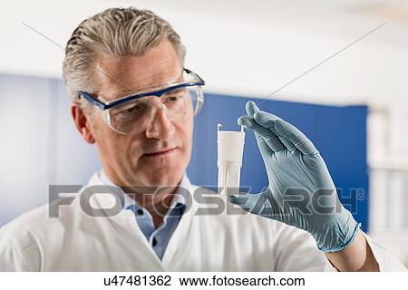 Stock Image - Scientist looking at container in laboratory. Fotosearch